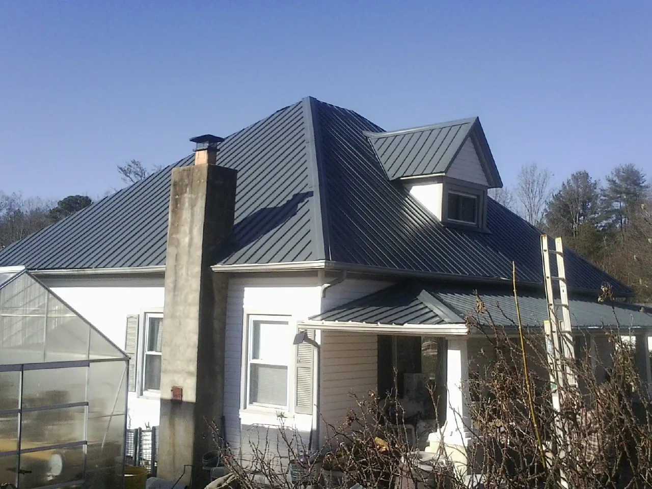 Dark blue standing seam metal roof on a white farmhouse with dormer — Slate & Tile Roof Repair by Roofing Brothers in Rancho Mirage