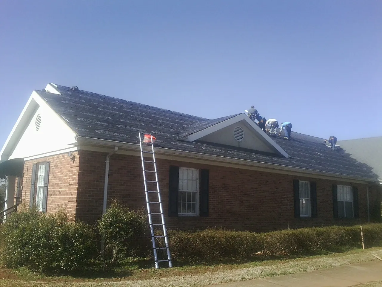 Crew tearing shingles off a brick ranch roof with a ladder set — Emergency Roof Repair work by our crew in Rancho Mirage