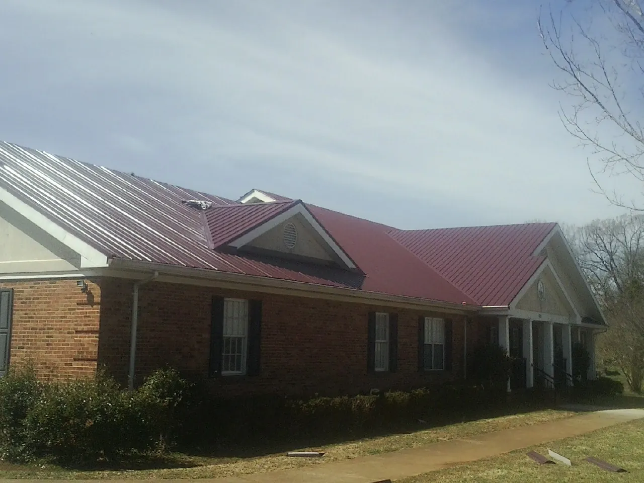 Red metal roof with gabled entries on a long brick building, from a Hail Damage Roof Repair job in Rancho Mirage
