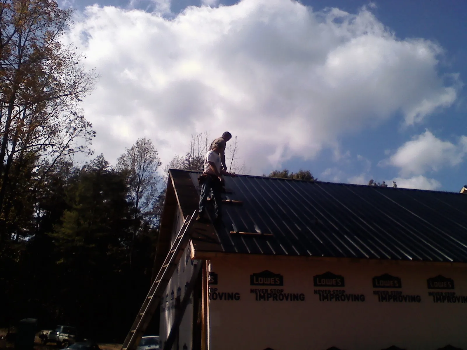 Roofer fastening dark metal panels high against a cloudy sky, from a Roof Inspection job in Rancho Mirage